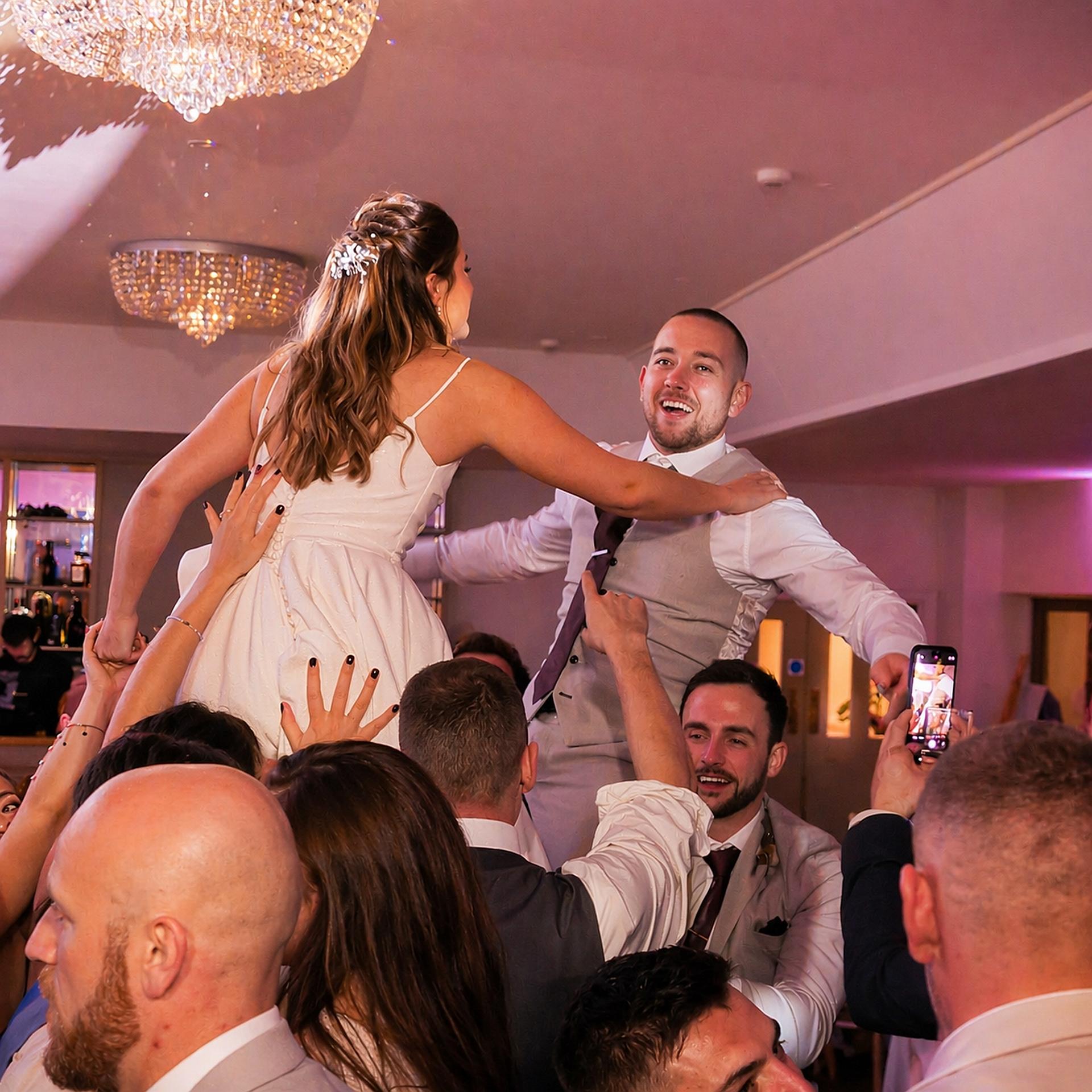 Bride and groom lifted above the crowd during a lively wedding celebration